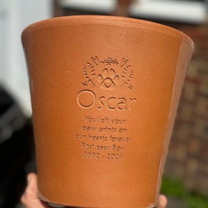 May include: A terracotta flower pot with a paw print and the name "Oscar" engraved on it. The pot also has the inscription "You left your paw prints on our hearts forever. Rest easy Boy. 2002-2024".