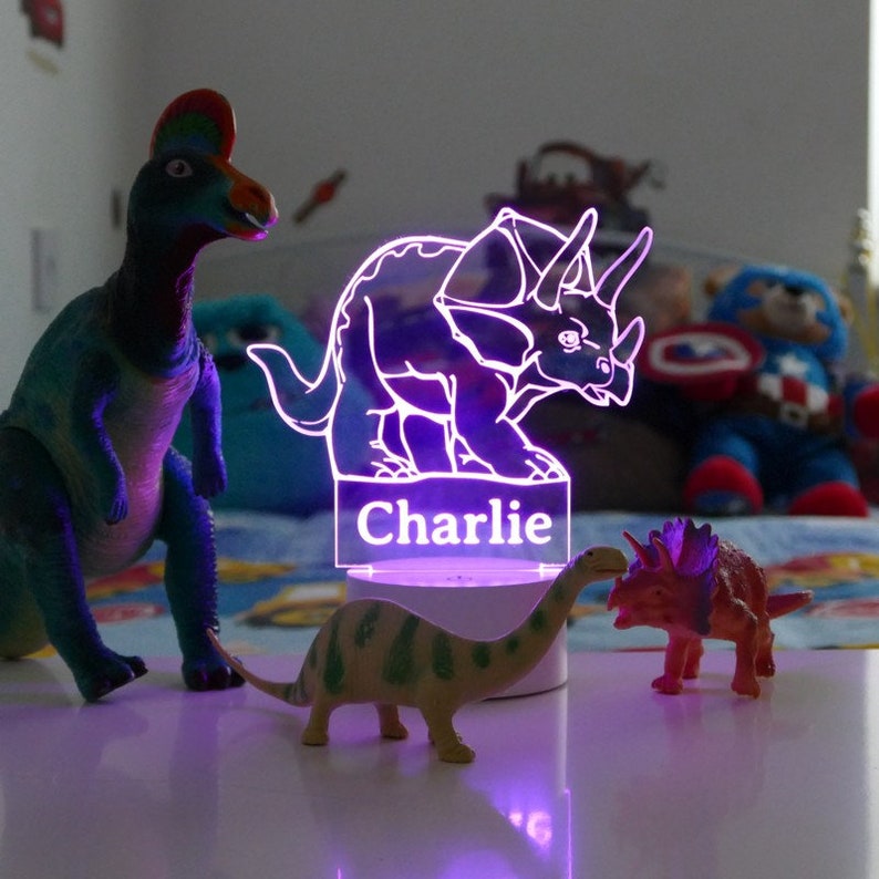 May include: A purple light-up dinosaur nightlight with the name "Charlie" on the base. The nightlight is surrounded by three toy dinosaurs.