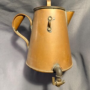 May include: A vintage copper coffee pot with a spout, handle, and lid. The pot has a warm, reddish-brown hue and a brass spigot. The handle is curved, and the lid has a small handle. The pot is likely used for brewing coffee.