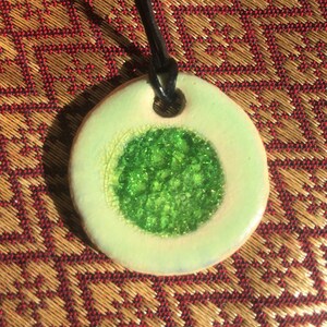 May include: A green and white ceramic pendant with a green glitter center, hanging from a black cord.