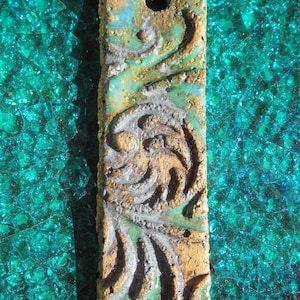 May include: A brown ceramic pendant with a blue and silver glaze. The pendant has a swirling design and is attached to a black cord.