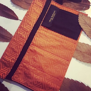 May include: A brown and black fabric roll-up case with a geometric pattern. The case has a black pocket with the text "Holly Unknown, Made in Ireland".