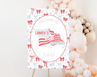 Pode incluir: Bem-vindo ao letreiro da festa de 1º aniversário da Lainey com um design de bandeira americana vermelha, branca e azul. O letreiro é decorado com laços rosa e azuis e estrelas em um fundo branco. A data 7.4.25 está impressa no letreiro.