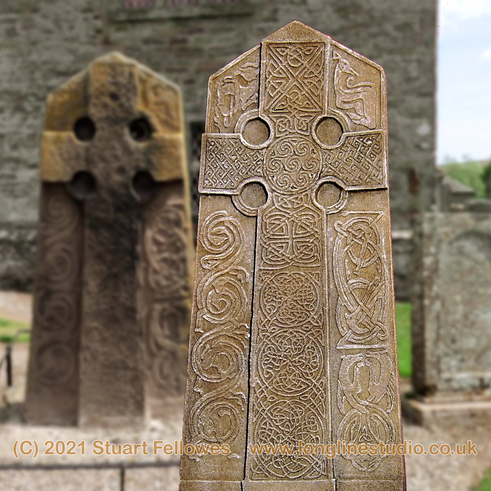 scale model of the Aberlemno Pictish Cross with Celtic designs in the foreground with the life size cross in the background