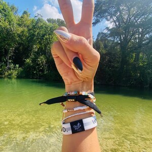 May include: A person's arm with black and white bracelets, including one that says "Truthfully" and another that says "W.O.W.". The person is making a peace sign with their hand, and their nails are painted black and silver.