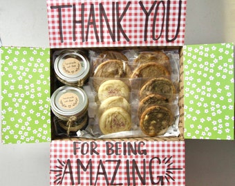 May include: A red and white checkered gift box with the words "Thank You" and "For Being Amazing" written in black marker. The box contains two jars of homemade jam and a variety of cookies.