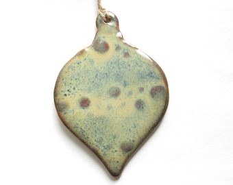 May include: A teardrop-shaped ceramic ornament with a speckled glaze in shades of green, yellow, and brown. The ornament has a hole at the top for hanging.