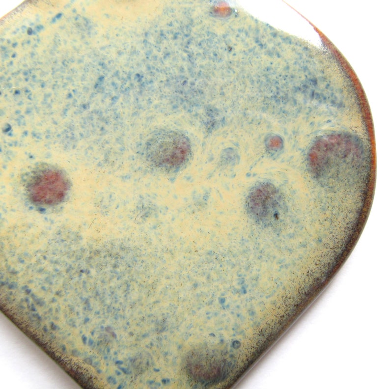 Peut inclure: Gros plan sur une tuile en c&eacute;ramique avec un fond jaune clair et des mouchetures bleues et brunes. La tuile a un bord arrondi et une surface l&eacute;g&egrave;rement irr&eacute;guli&egrave;re.