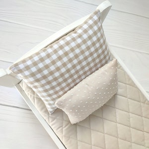Op de afbeelding: Een wit poppenbed met een beige, gestikte matras, een beige en wit geruit kussen en een beige kussen met witte stippen.