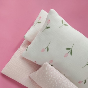 May include: Three pillows with floral patterns. The top pillow is white with pink flowers and green stems. The middle pillow is pink with a subtle texture. The bottom pillow is white with a small pink floral pattern.