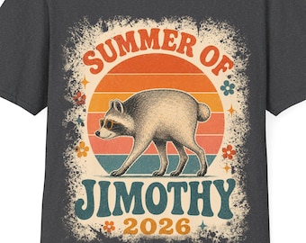 May include: A dark gray t-shirt featuring a graphic of a raccoon wearing sunglasses. The design includes a sunset background, small flowers, and the text "SUMMER OF JIMOTHY 2026" in a retro font. The print has a distressed, weathered appearance.