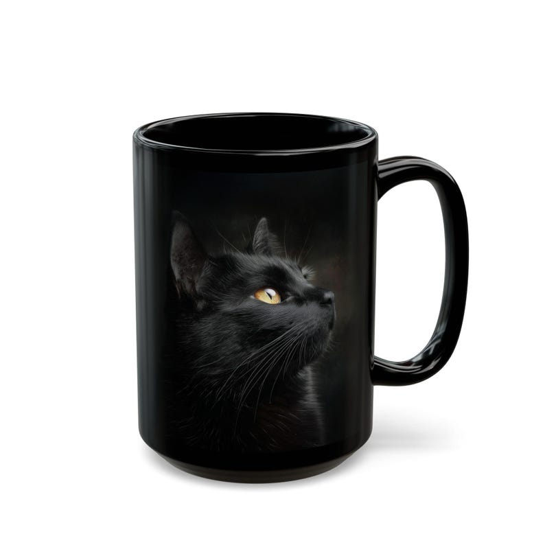 Pu&ograve; includere: Tazza in ceramica nera con un ritratto dettagliato di un gatto nero con occhi giallo brillante. Il gatto guarda verso l'alto, con i suoi baffi e la sua pelliccia chiaramente visibili. La tazza ha un manico grande.