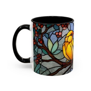 Puede incluir: Taza de cer&aacute;mica blanca con asa e interior negros. La taza presenta un dise&ntilde;o de vidriera de un p&aacute;jaro amarillo posado en una rama con bayas rojas y hojas verdes. El fondo tiene tonos azules y grises.