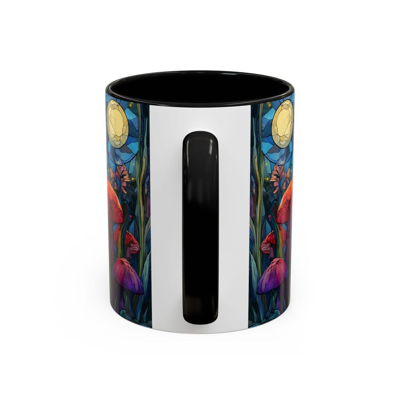 Peut inclure: Une tasse &agrave; caf&eacute; en c&eacute;ramique avec un int&eacute;rieur et une anse noirs, et un ext&eacute;rieur blanc. La tasse pr&eacute;sente une illustration color&eacute;e de champignons, de plantes et d'une lune. Le design est dans les tons de rouge, violet, bleu et jaune.
