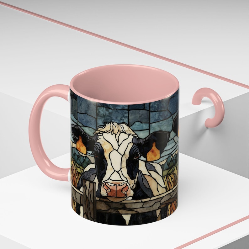 Puede incluir: Una taza de cer&aacute;mica con asa e interior rosas. El exterior presenta una ilustraci&oacute;n de vaca estilo vidriera mirando por encima de una valla. La vaca es negra, blanca y marr&oacute;n, con una nariz rosa.