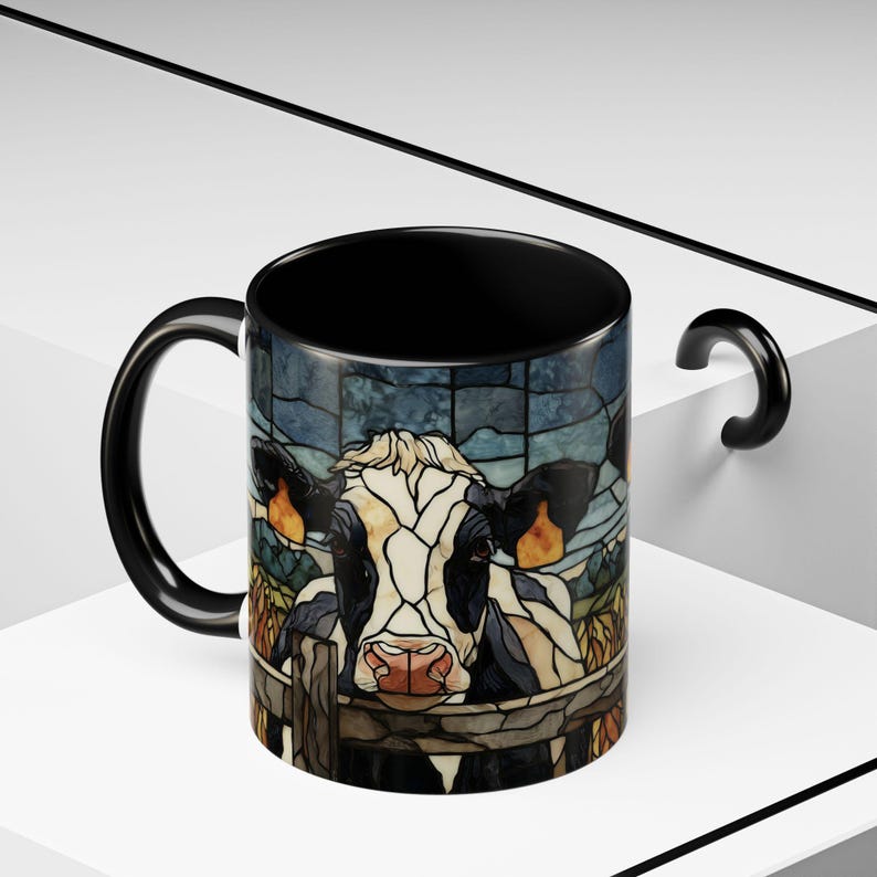 Puede incluir: Taza de cer&aacute;mica negra con un dise&ntilde;o de vaca estilo vidriera. La vaca es blanca y negra con una nariz rosada, mirando por encima de una valla de madera. La taza tiene interior y asa negros.