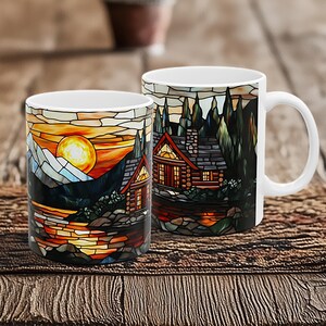 May include: Two white ceramic mugs with a stained glass design of a cabin in the woods at sunset. The design features a log cabin with a stone chimney, trees, and a lake with a reflection of the setting sun.