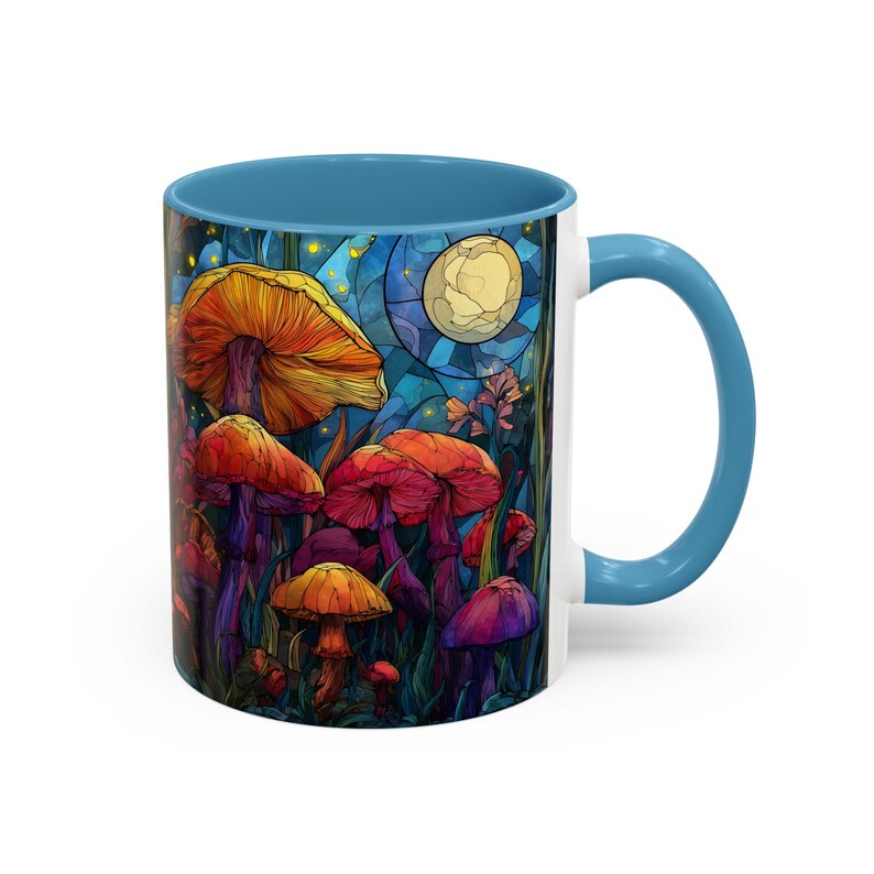 Peut inclure: Une tasse en c&eacute;ramique blanche avec un int&eacute;rieur et une anse bleus. La tasse pr&eacute;sente une illustration color&eacute;e de champignons dans un cadre forestier, avec une pleine lune en arri&egrave;re-plan. Les champignons sont de couleurs vari&eacute;es, dont orange, rouge et violet.