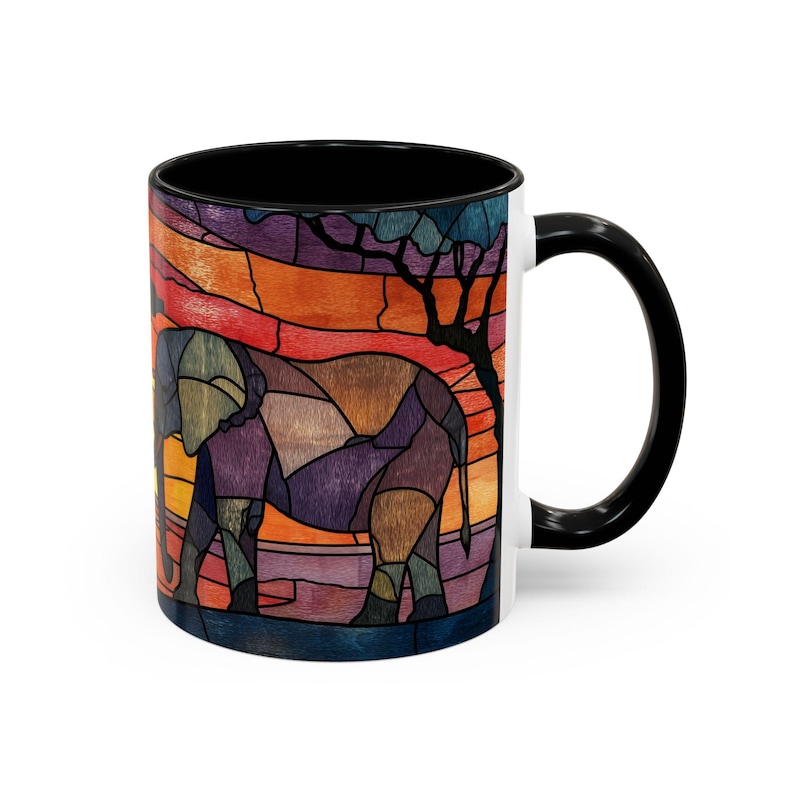 Puede incluir: Una taza de cer&aacute;mica con asa e interior negros. La taza presenta un dise&ntilde;o de vidriera de una silueta de elefante sobre un fondo de puesta de sol con tonos naranja, rojo y p&uacute;rpura. Tambi&eacute;n se ve un &aacute;rbol.