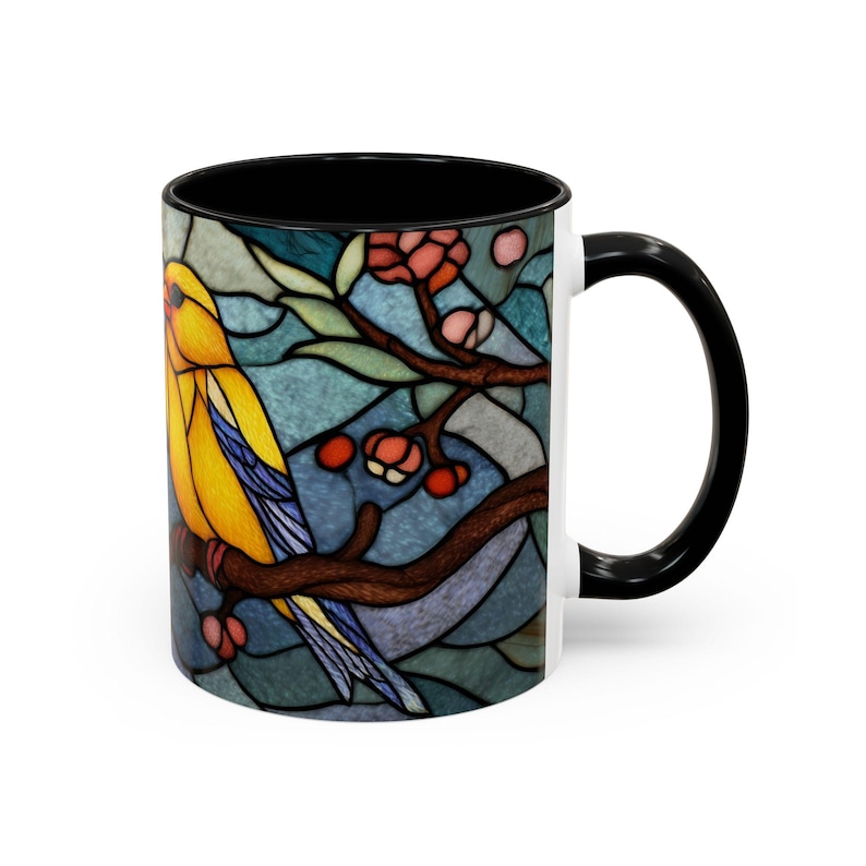 Puede incluir: Taza de cer&aacute;mica blanca con interior y asa negros. La taza presenta un dise&ntilde;o de vidriera de un p&aacute;jaro amarillo posado en una rama con bayas rojas sobre un fondo azul.