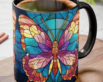 May include: Black coffee mug featuring a stained-glass butterfly design. The butterfly has colorful wings in shades of blue, purple, yellow, and orange. The mug has a black handle and rim, and is filled with coffee.