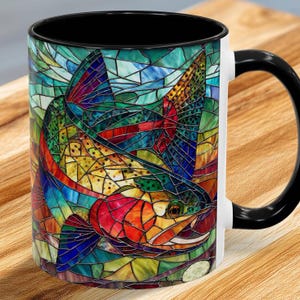 May include: White ceramic mug with a black handle and rim. The mug features a colorful stained-glass design of a fish in shades of red, orange, yellow, green, blue, and purple. The design wraps around the mug.