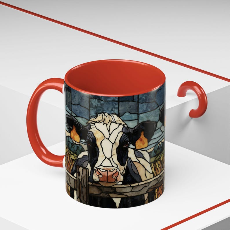Puede incluir: Una taza de caf&eacute; de cer&aacute;mica con interior y asa rojos. El exterior presenta una imagen de estilo vidriera de una vaca mirando por encima de una valla. La vaca es negra, blanca y marr&oacute;n, con una nariz rosa. El fondo es azul y verde.