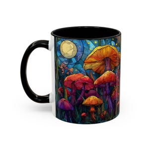 Peut inclure: Mug en c&eacute;ramique blanche avec une anse et un int&eacute;rieur noirs. La tasse pr&eacute;sente une illustration color&eacute;e de champignons dans un cadre forestier sous une pleine lune. Les champignons sont dans des tons orange, rouge et violet.