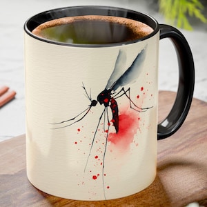 May include: A ceramic coffee mug with a black handle and rim. The mug features a watercolor illustration of a mosquito with red and black accents. The background is a cream color.