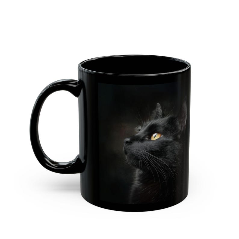 Pu&ograve; includere: Tazza in ceramica nera con l'immagine di un gatto nero con occhi giallo brillante. Il gatto guarda di lato su uno sfondo scuro. La tazza ha un manico curvo.