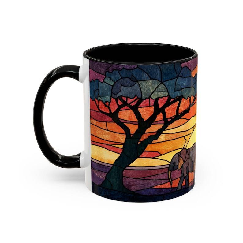Puede incluir: Taza de cer&aacute;mica blanca con asa e interior negros. La taza presenta un dise&ntilde;o de estilo vidriera de una escena de sabana africana con un &aacute;rbol, un elefante y una puesta de sol en tonos naranja, amarillo, morado y azul.