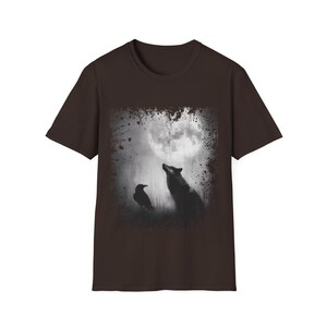 Pu&ograve; includere: T-shirt marrone con girocollo e grafica. Il design presenta un'immagine in bianco e nero di un lupo che ulula alla luna, con un corvo in primo piano. La maglietta ha maniche corte.