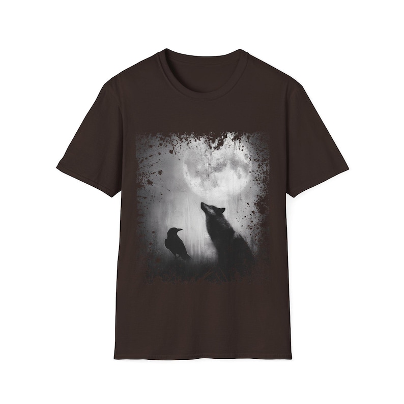 Pu&ograve; includere: T-shirt marrone con girocollo e grafica. Il design presenta un'immagine in bianco e nero di un lupo che ulula alla luna, con un corvo in primo piano. La maglietta ha maniche corte.