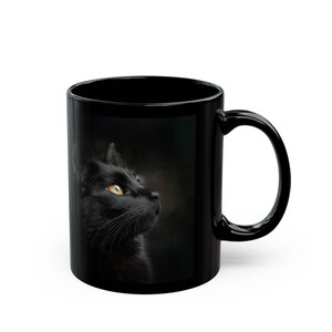 Pu&ograve; includere: Tazza in ceramica nera con il profilo laterale di un gatto nero con occhi gialli. Il gatto &egrave; posto su uno sfondo scuro. La tazza ha un manico curvo.