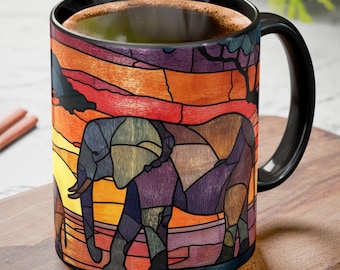 May include: A black-handled coffee mug featuring a stained-glass style design of an elephant walking across an African sunset. The mug's design incorporates shades of orange, yellow, purple, and blue. The mug is filled with a dark liquid.