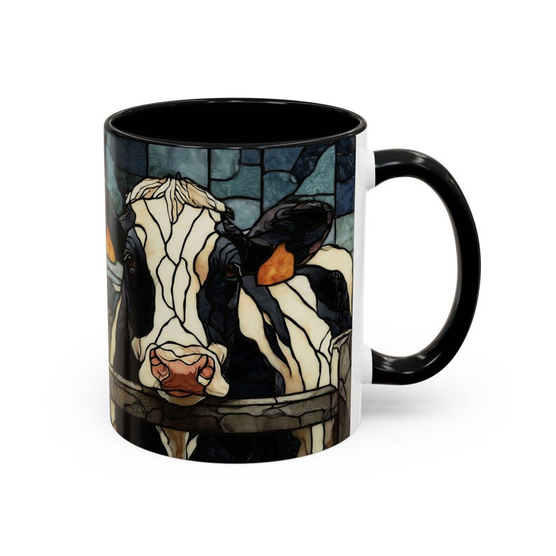 Puede incluir: Una taza de cer&aacute;mica blanca con interior y asa negros. La taza presenta una colorida ilustraci&oacute;n de estilo vidriera del rostro de una vaca. La vaca es blanca y negra con una nariz rosada y est&aacute; detr&aacute;s de una valla de madera.