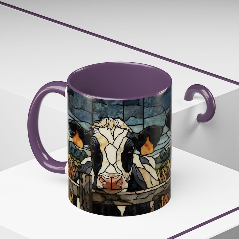 Puede incluir: Una taza de caf&eacute; de cer&aacute;mica con un dise&ntilde;o de vaca estilo vidriera. La taza tiene un interior y un asa morados, y el gr&aacute;fico de la vaca es en negro, blanco, marr&oacute;n y beige. La vaca est&aacute; detr&aacute;s de una valla de madera.