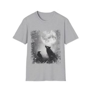 Pu&ograve; includere: T-shirt grigio con un'illustrazione in bianco e nero di un lupo che ulula alla luna piena, con un corvo nelle vicinanze. Il design ha un'estetica vintage e usurata, con un bordo strutturato attorno all'immagine.