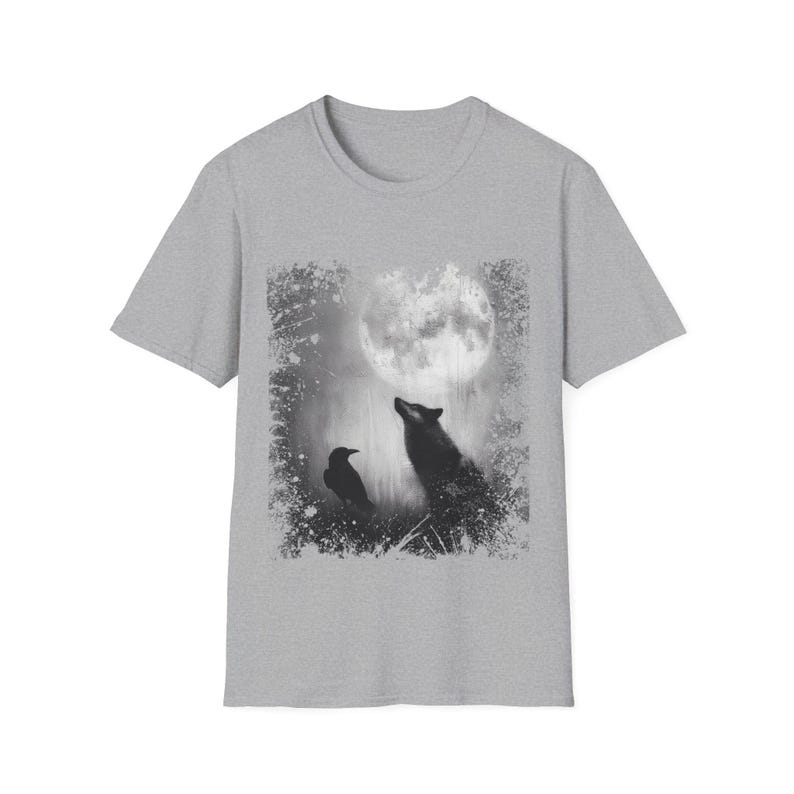 Pu&ograve; includere: T-shirt grigio con un'illustrazione in bianco e nero di un lupo che ulula alla luna piena, con un corvo nelle vicinanze. Il design ha un'estetica vintage e usurata, con un bordo strutturato attorno all'immagine.