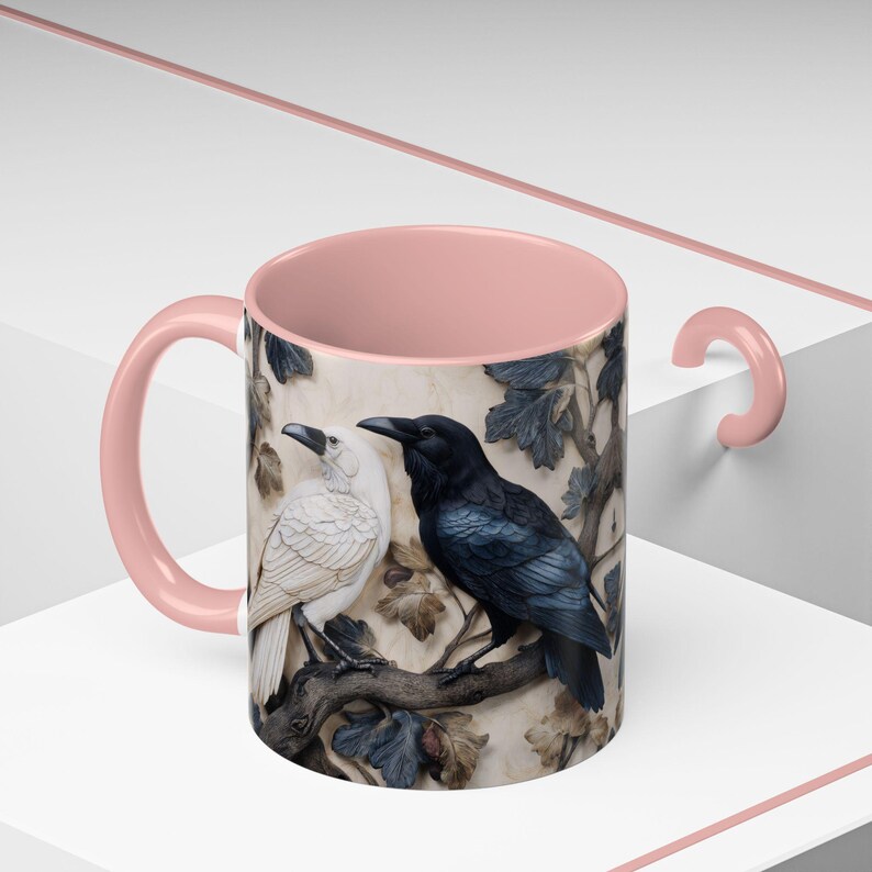 May include: A ceramic mug with a pink handle and interior. The exterior features a detailed relief of two birds, one white and one black, perched on a branch with leaves. The background has a textured, neutral tone.