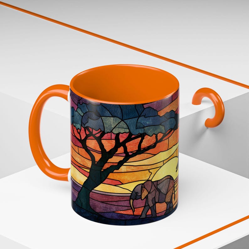 Puede incluir: Taza de cer&aacute;mica naranja con un dise&ntilde;o de vidriera de una sabana africana. El dise&ntilde;o incluye un &aacute;rbol, un elefante y una puesta de sol con tonos naranja, amarillo y morado. El asa y el interior de la taza tambi&eacute;n son naranjas.
