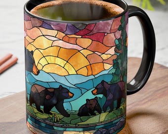 May include: Black coffee mug with a stained glass design featuring a family of bears in a forest scene. The mug has a black handle and rim, and the artwork includes a sunset with orange, yellow, and blue hues.
