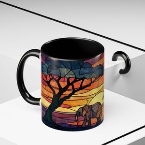 Puede incluir: Taza de cer&aacute;mica negra con un dise&ntilde;o de vidriera que representa una sabana africana. El dise&ntilde;o incluye un &aacute;rbol, un elefante y una puesta de sol en tonos naranja, amarillo y morado. La taza tiene un asa y un interior negros.