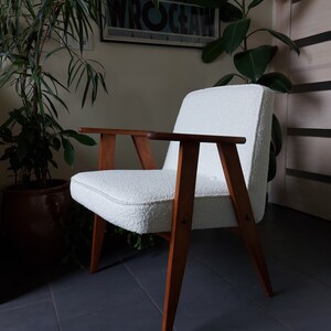 May include: A white armchair with a fluffy, textured fabric upholstery. The chair has a wooden frame with a dark brown finish and angled legs.