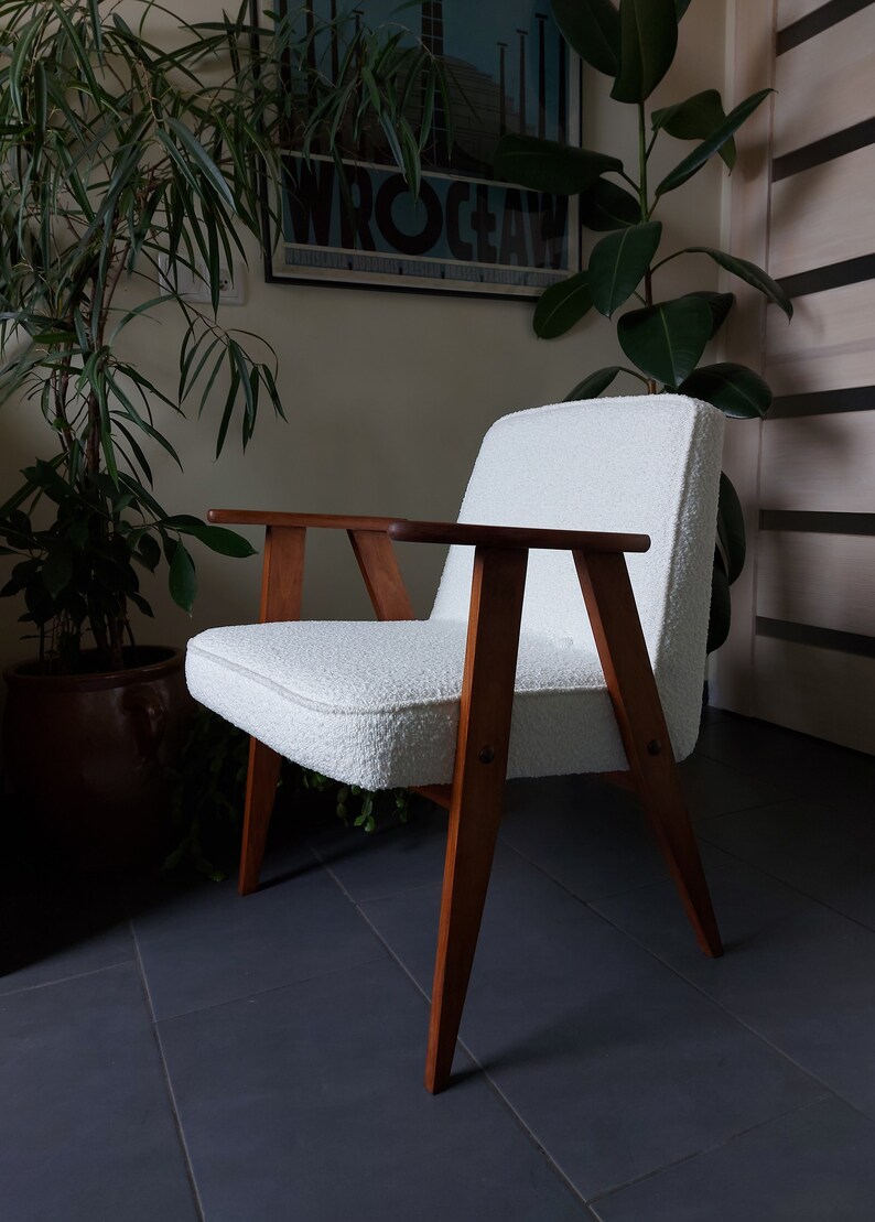 May include: A white armchair with a fluffy, textured fabric upholstery. The chair has a wooden frame with a dark brown finish and angled legs.