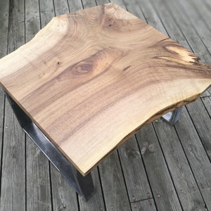 Könnte beinhalten: Ein Holz-Couchtisch mit einer Live-Edge-Platte und einem Metallgestell. Der Tisch hat eine natürliche Holzoptik und eine einzigartige Form.