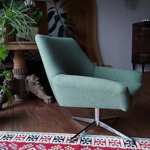 May include: A green swivel chair with a chrome base. The chair is upholstered in a soft, textured fabric. The chair is sitting on a rug with a colourful geometric pattern.