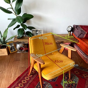 May include: A mustard yellow armchair with wooden legs and arms. The chair is 43 cm wide, 61.5 cm tall, and 51 cm deep. The seat is 41 cm wide and 36 cm deep.