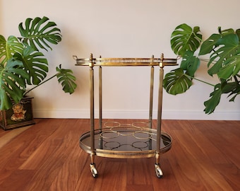 Golden trolley bar cart, Mid-Century oval two-tier service trolley, removable tray, bottle holder, polished brass, smoked glass, the Fifties