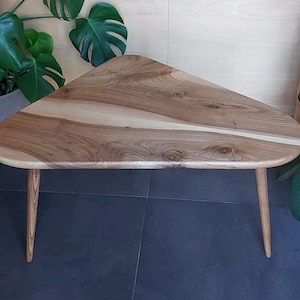 Puede incluir: Una mesa de centro triangular de madera con un acabado de madera natural y un patrón de veta único. La mesa tiene tres patas y está hecha de madera maciza.